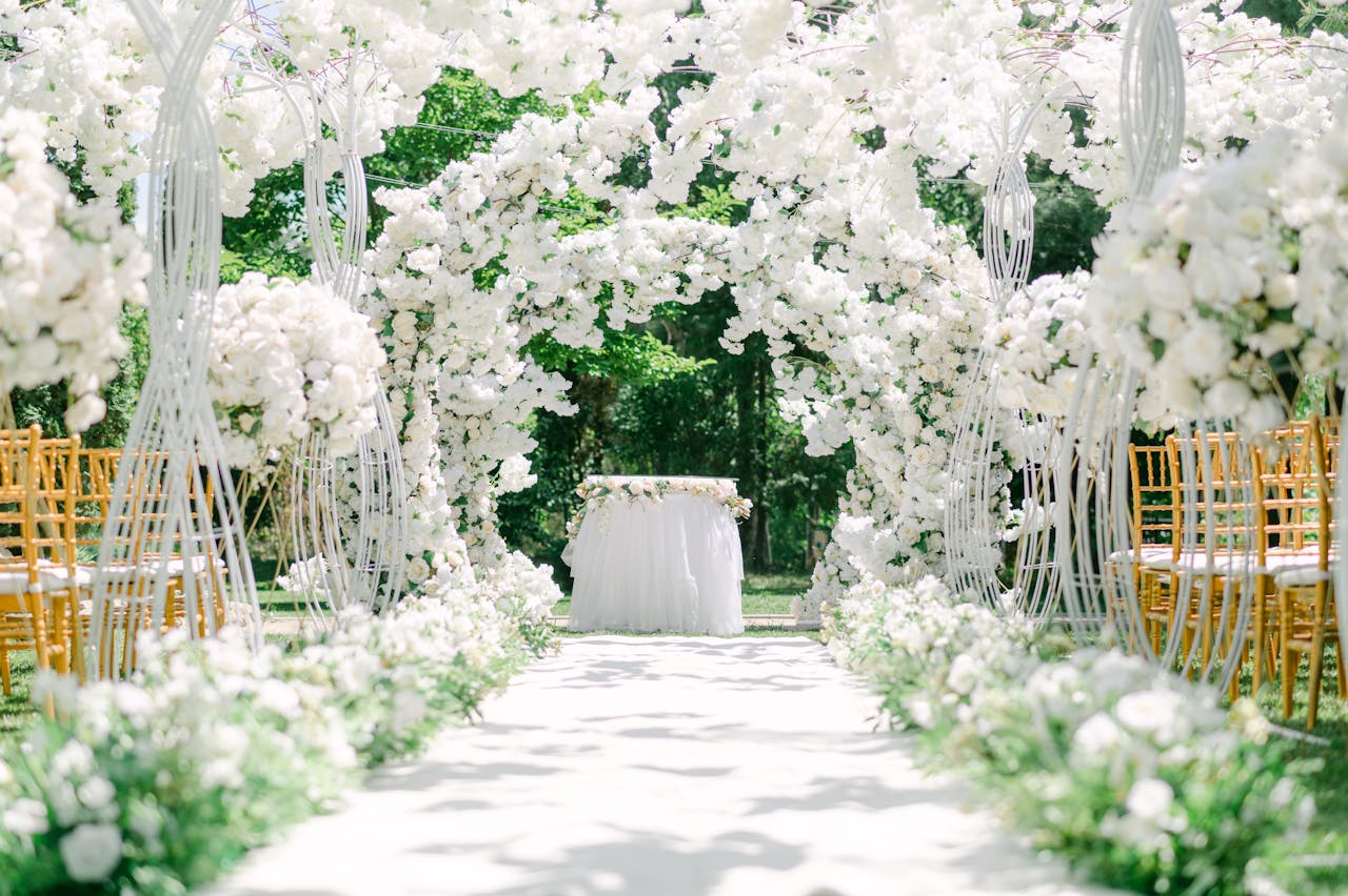 Home An elegant outdoor wedding venue setup with white floral arches and chairs.