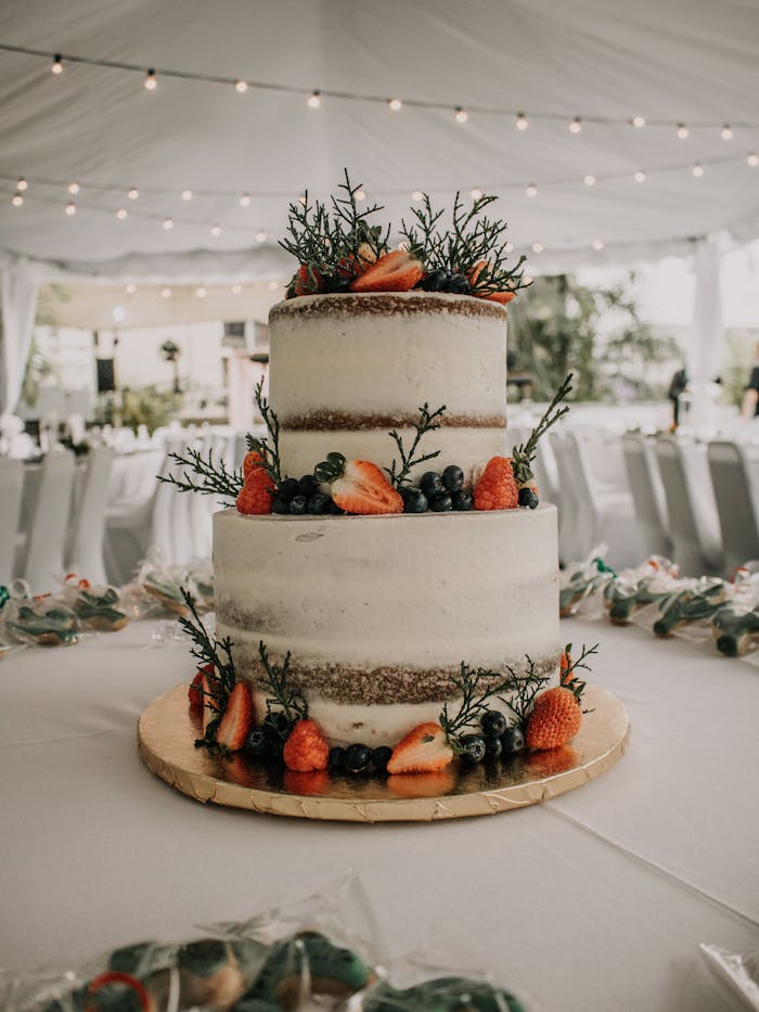 A two-tier naked wedding cake adorned with fresh strawberries and blueberries in a decorated reception tent.